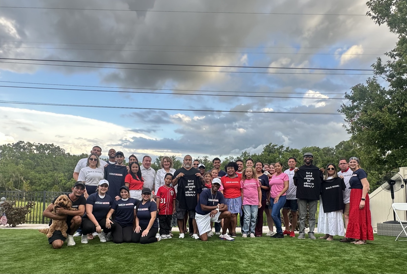 A large group gathered outdoors wearing Role Model t-shirts, some holding shirts reading Set a good example for others to follow