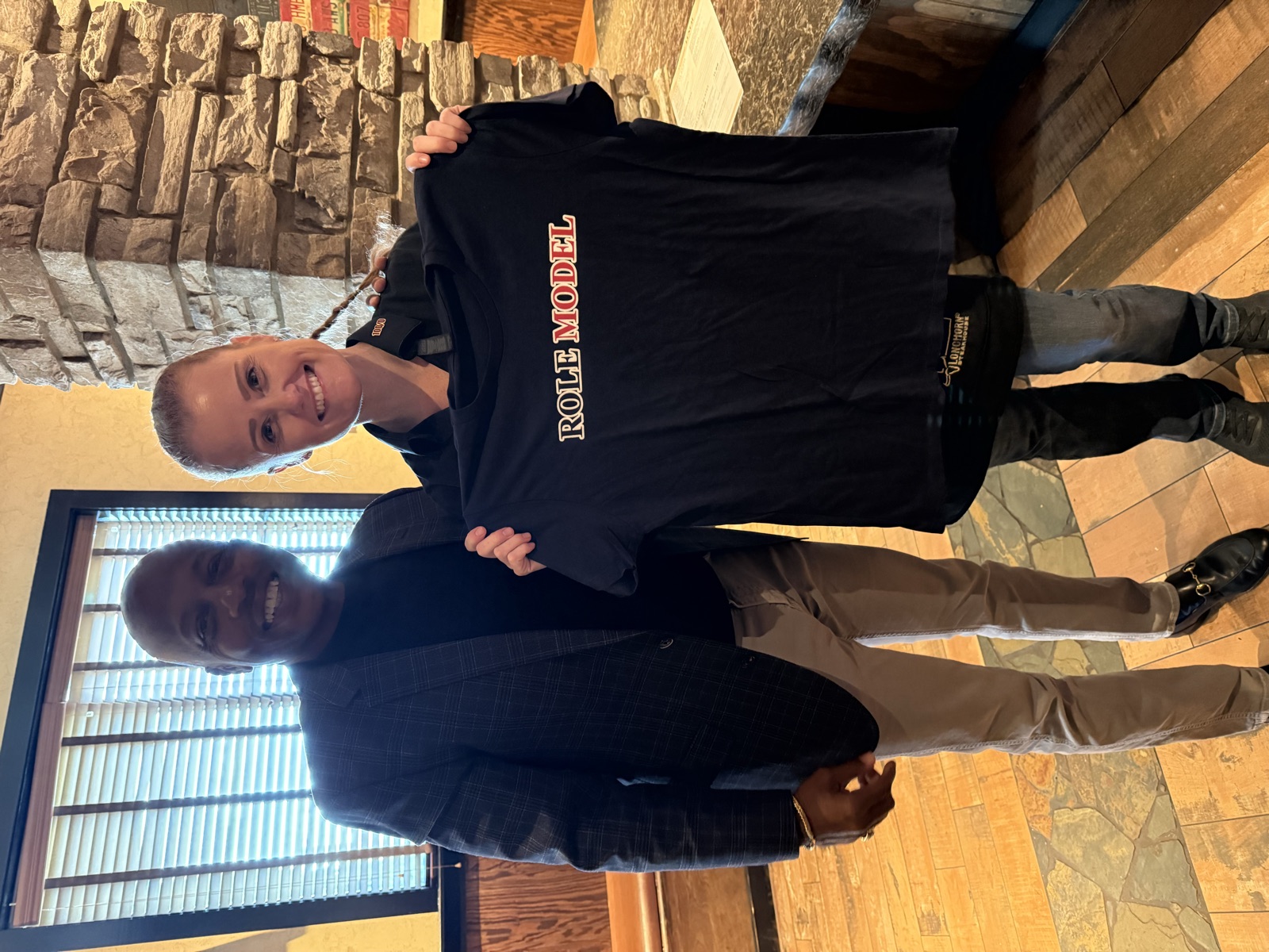 A man in a blazer and a Longhorn restaurant employee holding up a navy Role Model t-shirt