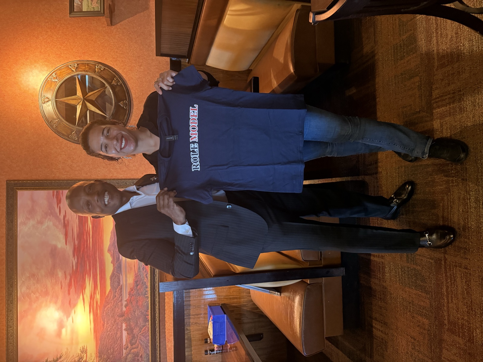 A man in a suit and a Longhorn restaurant server holding up a navy Role Model t-shirt