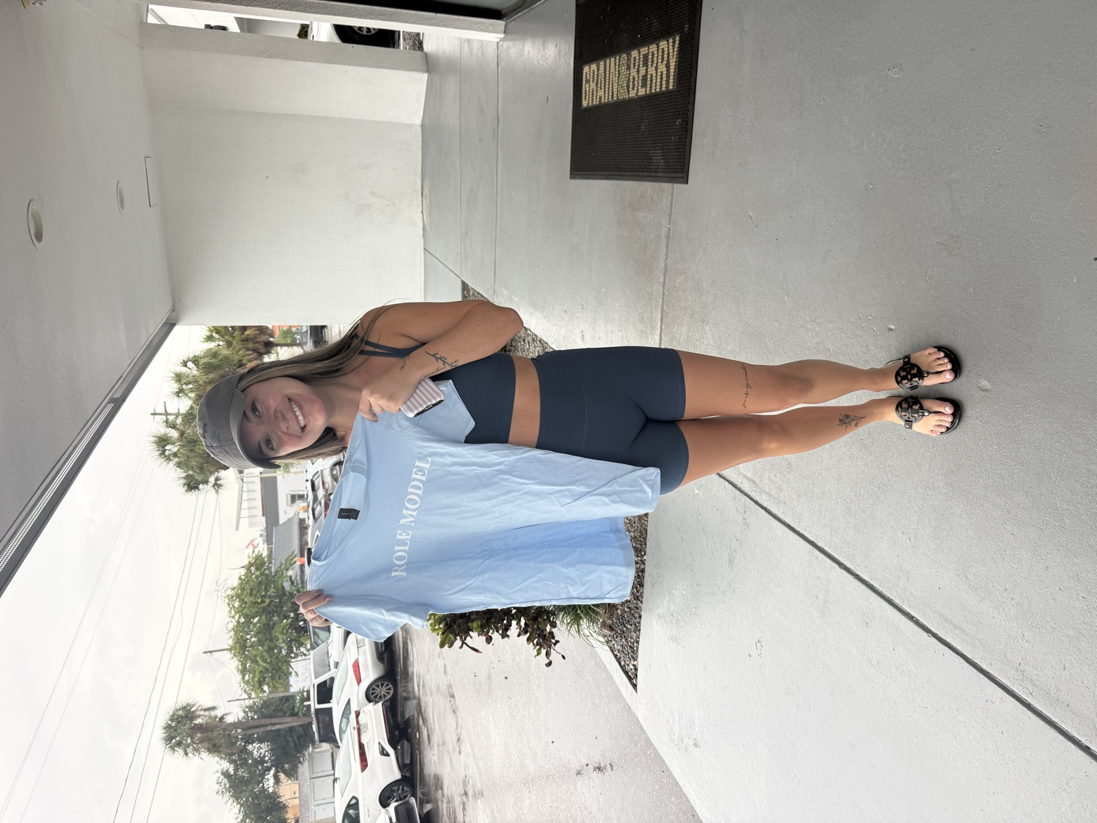 A smiling woman holding up a light-blue Role Model t-shirt