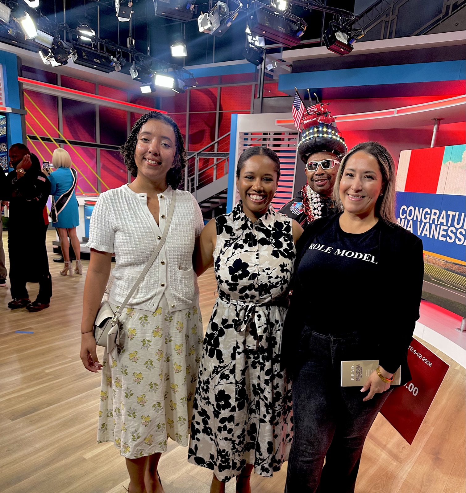 A Role Models Foundation representative in a Role Model shirt at a TV studio, holding the R.E.A.D. Mentoring and Intervention Program book